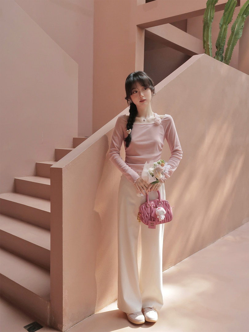 Model wearing a pink long-sleeve top and white wide-leg pants holding a pink handbag