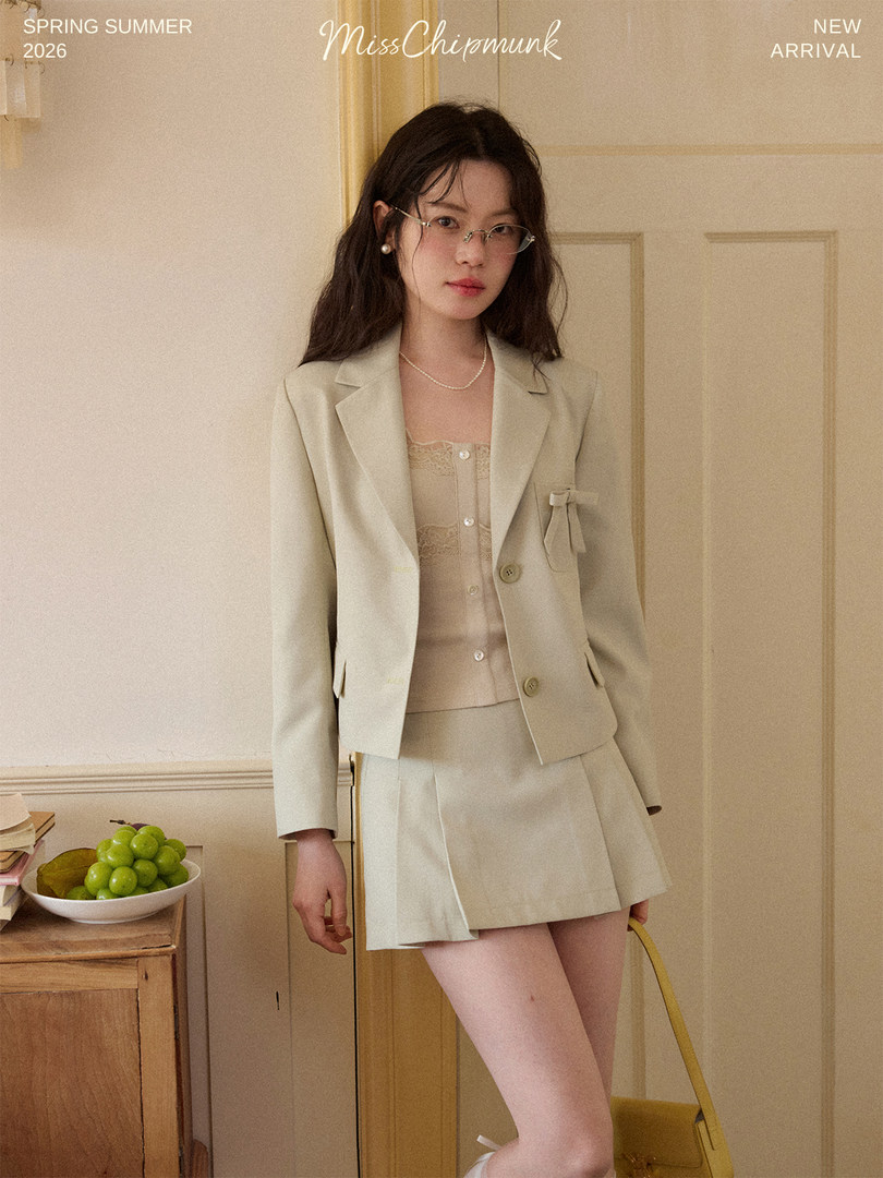 Woman wearing a cream blazer and pleated mini skirt set