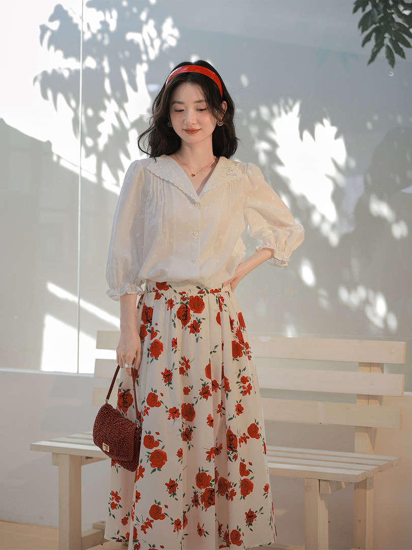 Woman wearing a white blouse and red floral midi skirt with a handbag