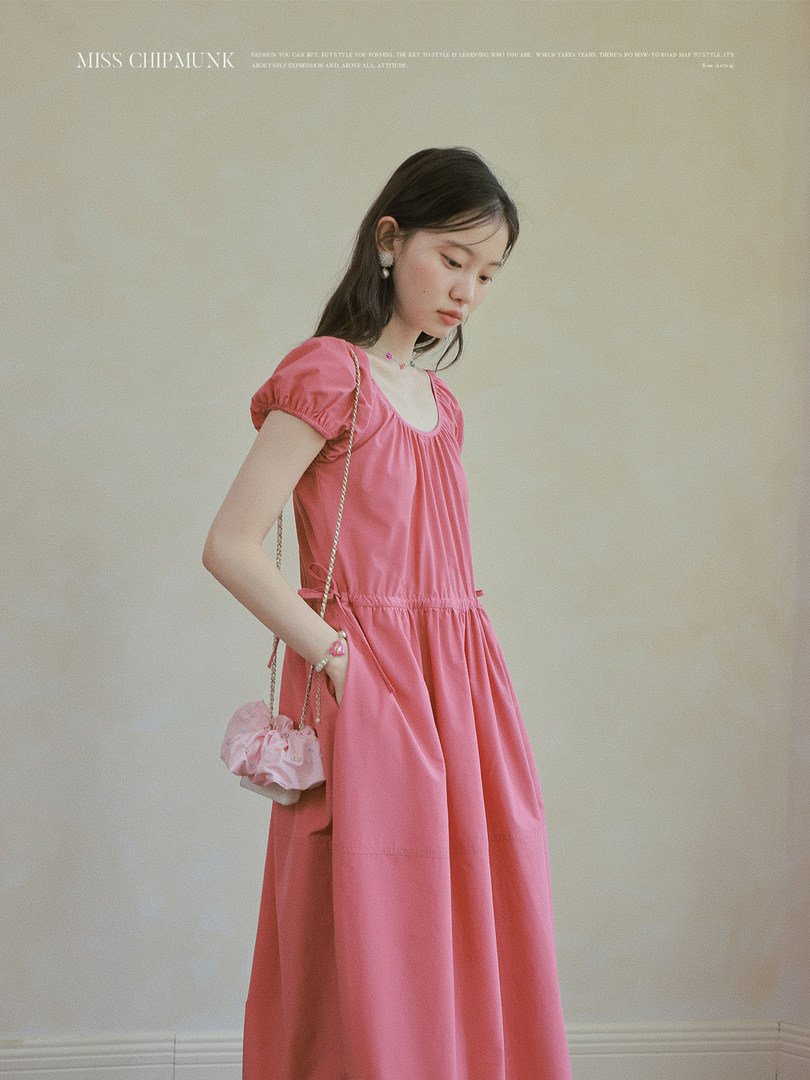 Model wearing a pink short-sleeve dress with a gathered waist and crossbody bag