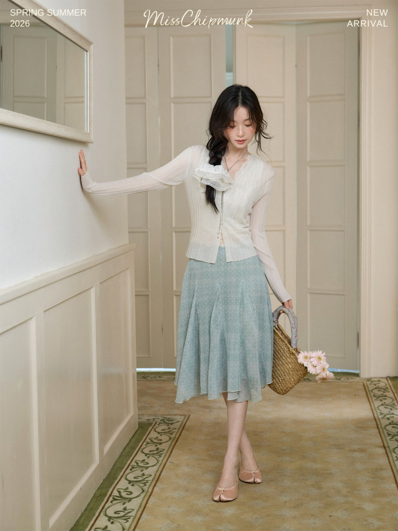 Woman wearing a white cardigan with a light blue midi skirt and straw bag