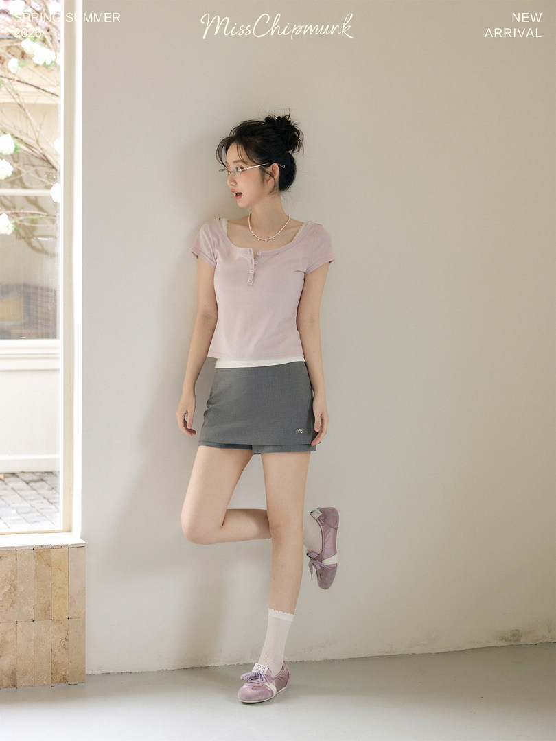 Model wearing a light pink short-sleeve top with a gray mini skirt and lilac sneakers
