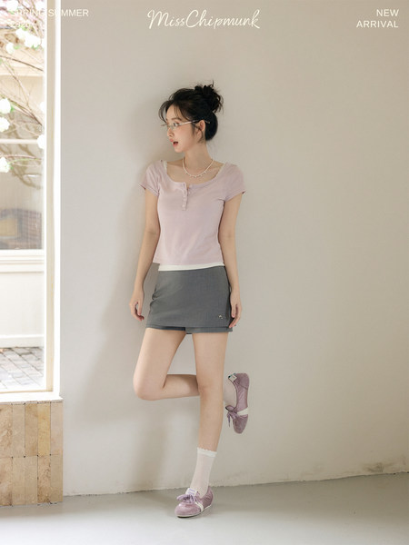Model wearing a light pink short-sleeve top with a gray mini skirt and lilac sneakers