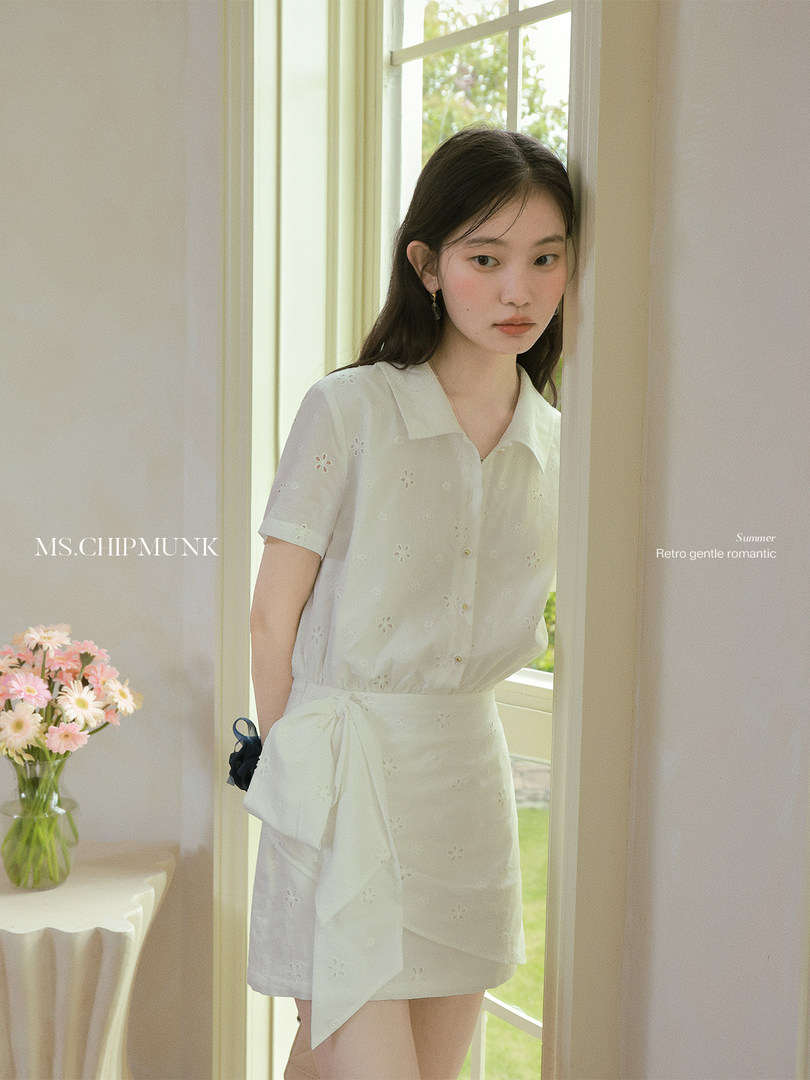 Model wearing a white embroidered short-sleeve blouse and matching wrap skirt