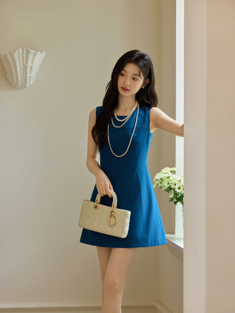 Woman wearing a sleeveless blue dress and holding a beige quilted handbag