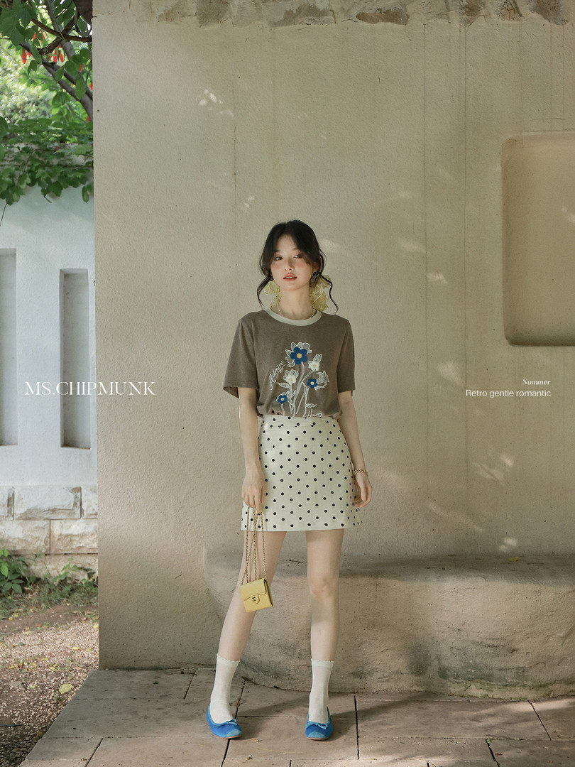 Model wearing a brown graphic T-shirt with a white polka dot mini skirt and blue flats