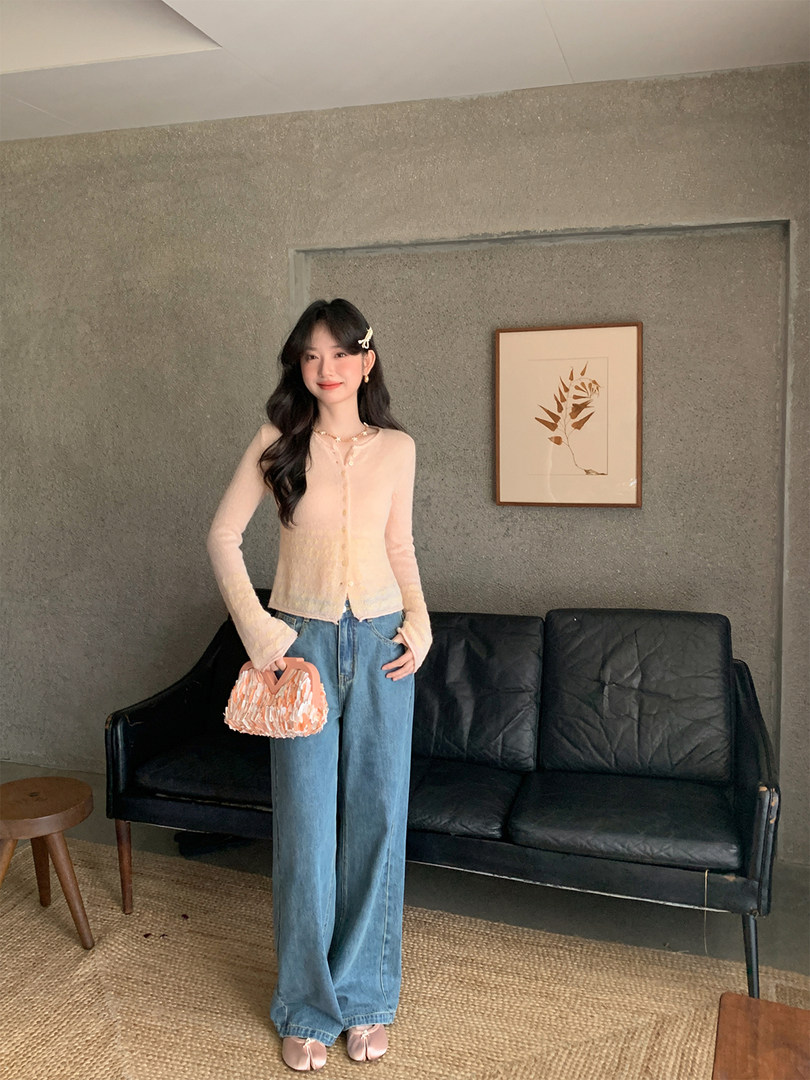 Woman wearing a light pink sheer cardigan with wide-leg jeans indoors