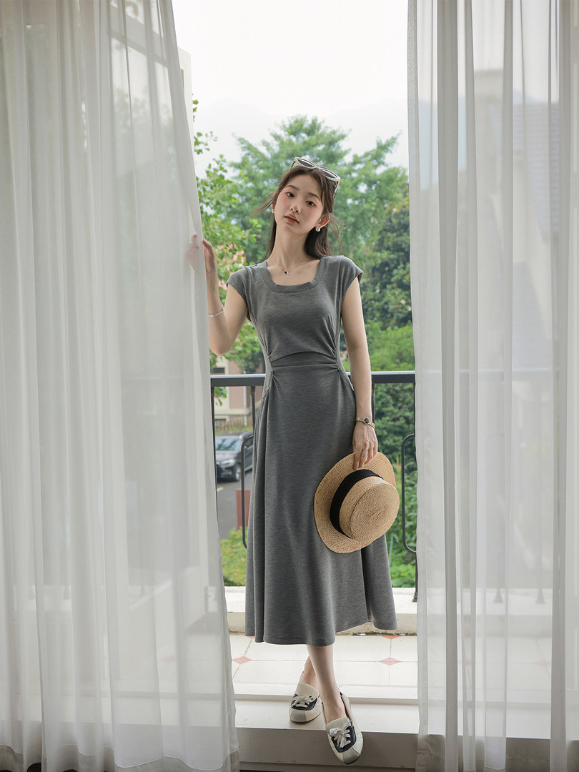 Woman wearing a gray sleeveless midi dress and holding a straw hat