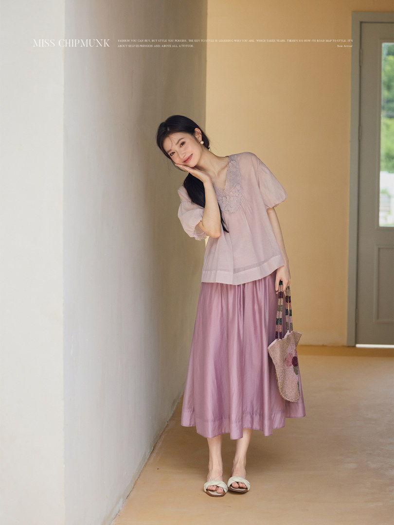 Woman wearing a light pink sheer blouse and midi skirt with sandals and a small tote bag