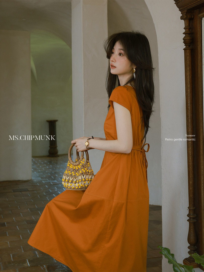 Woman wearing an orange sleeveless midi dress holding a woven handbag