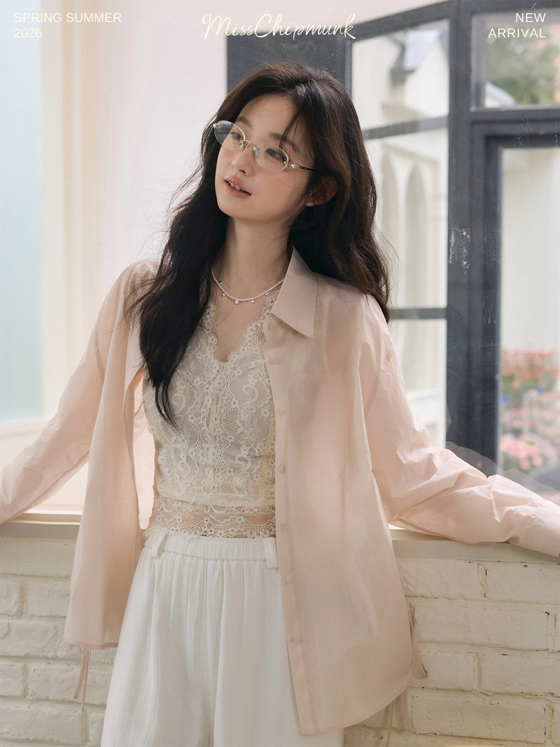 Model wearing a light pink shirt over a lace camisole with white skirt in a bright indoor setting