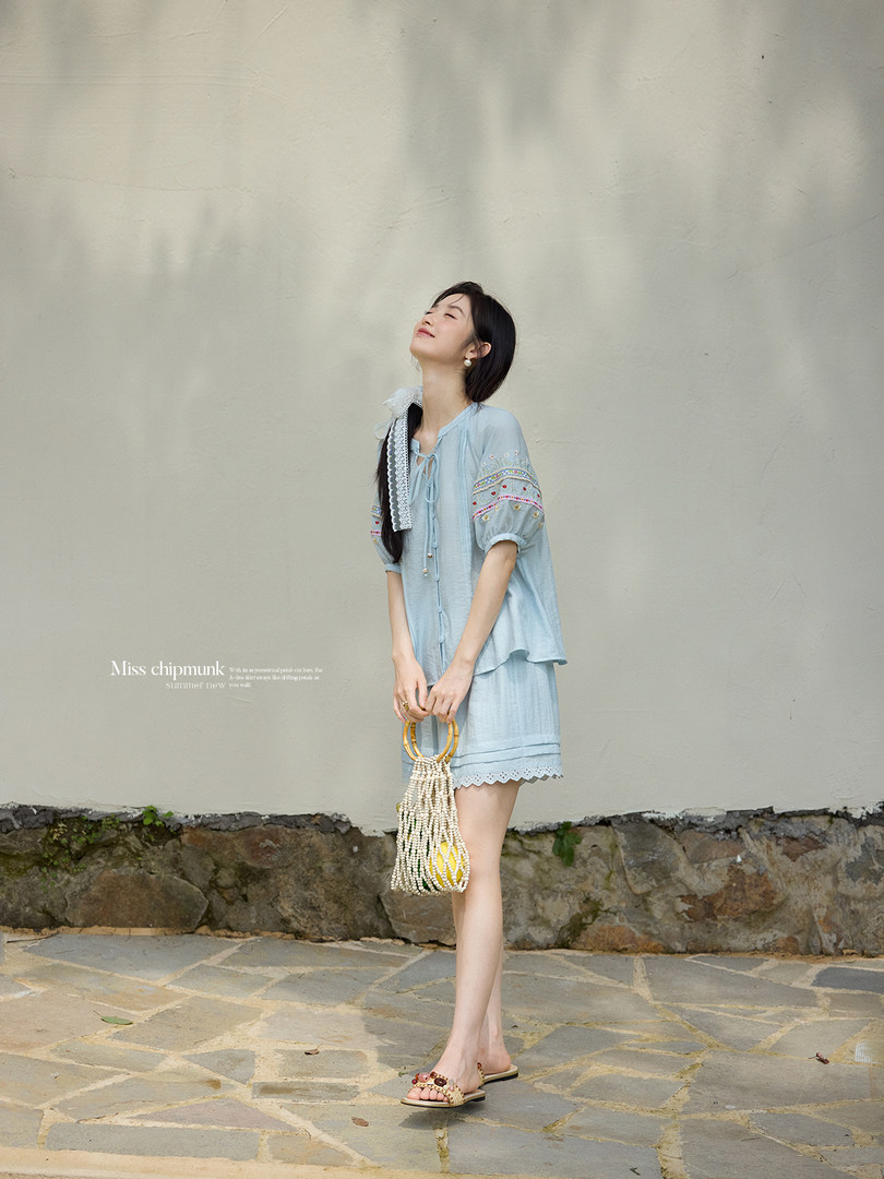 Model wearing a light blue embroidered summer outfit with a beaded handbag and sandals