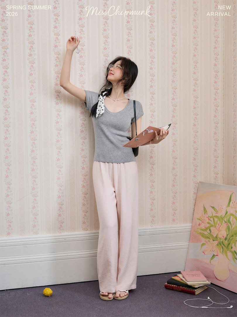 Model wearing a gray short-sleeve top and pale pink wide-leg pants in a studio setting