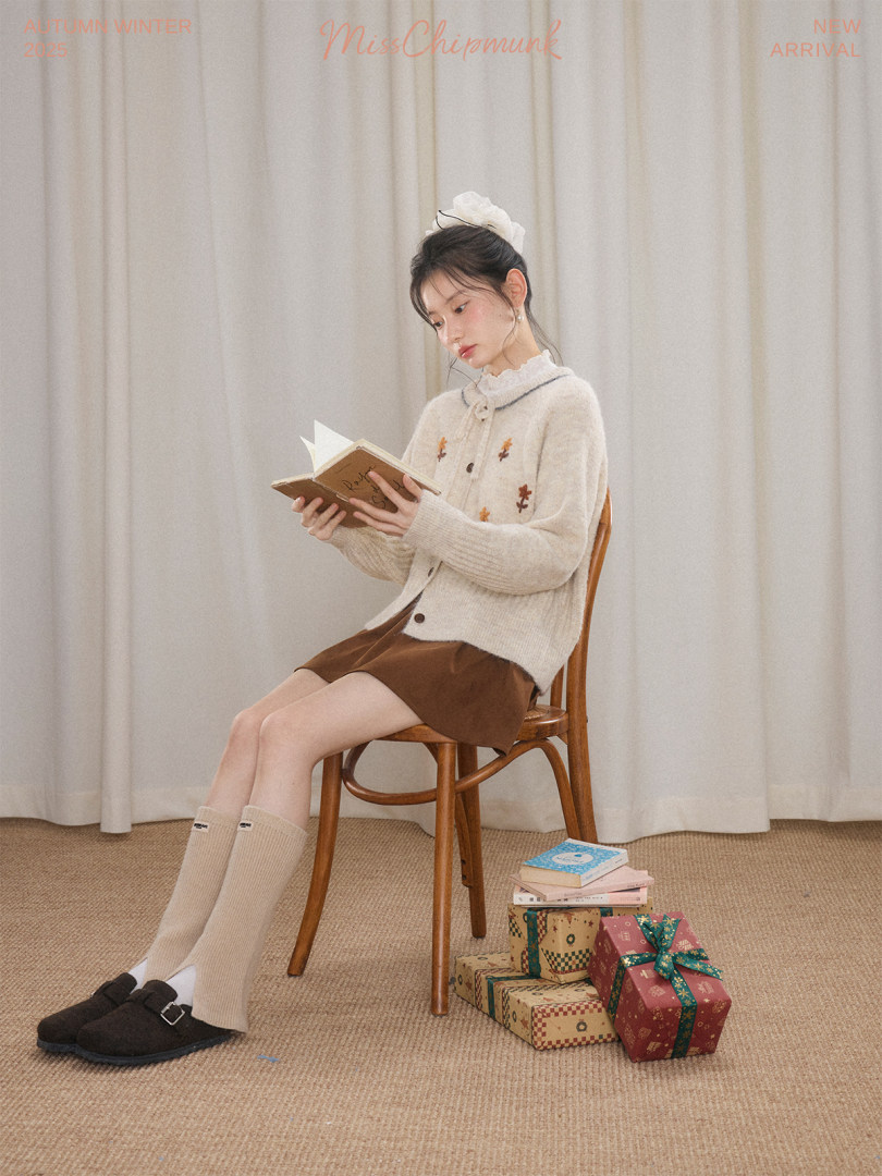 Young woman wearing a cream cardigan and brown skirt with knee-high socks, seated indoors