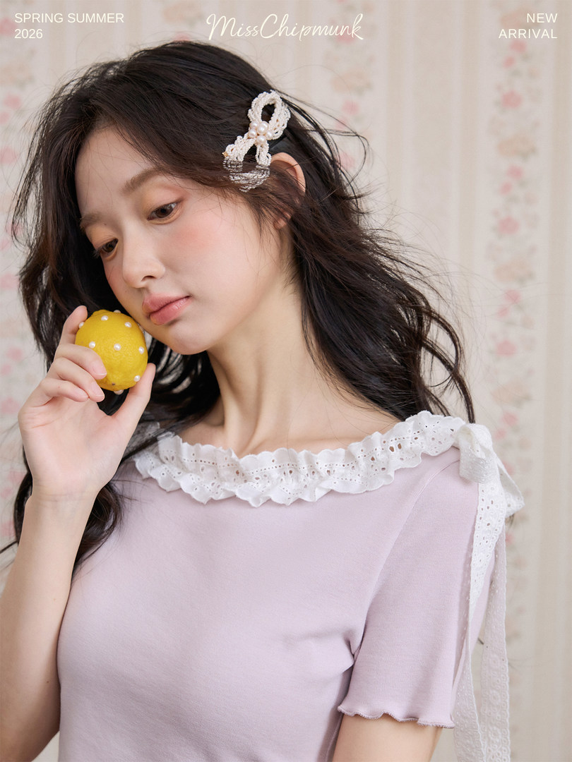 Young woman wearing a light pink ruffled short-sleeve top with pearl hair clip