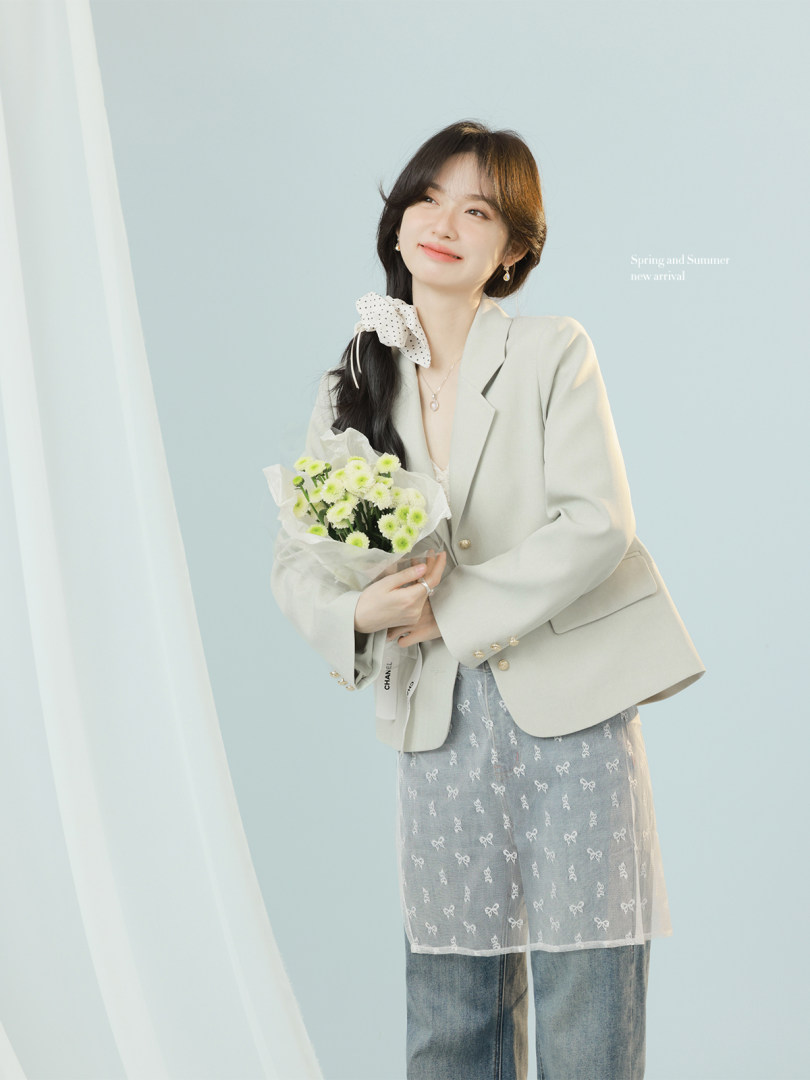 Woman wearing a light beige blazer outfit with a sheer bow-patterned skirt overlay, holding flowers