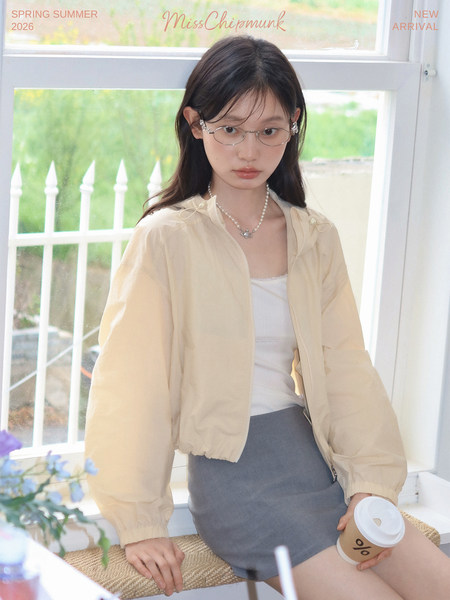 Model wearing a beige lightweight jacket over a white top and gray skirt