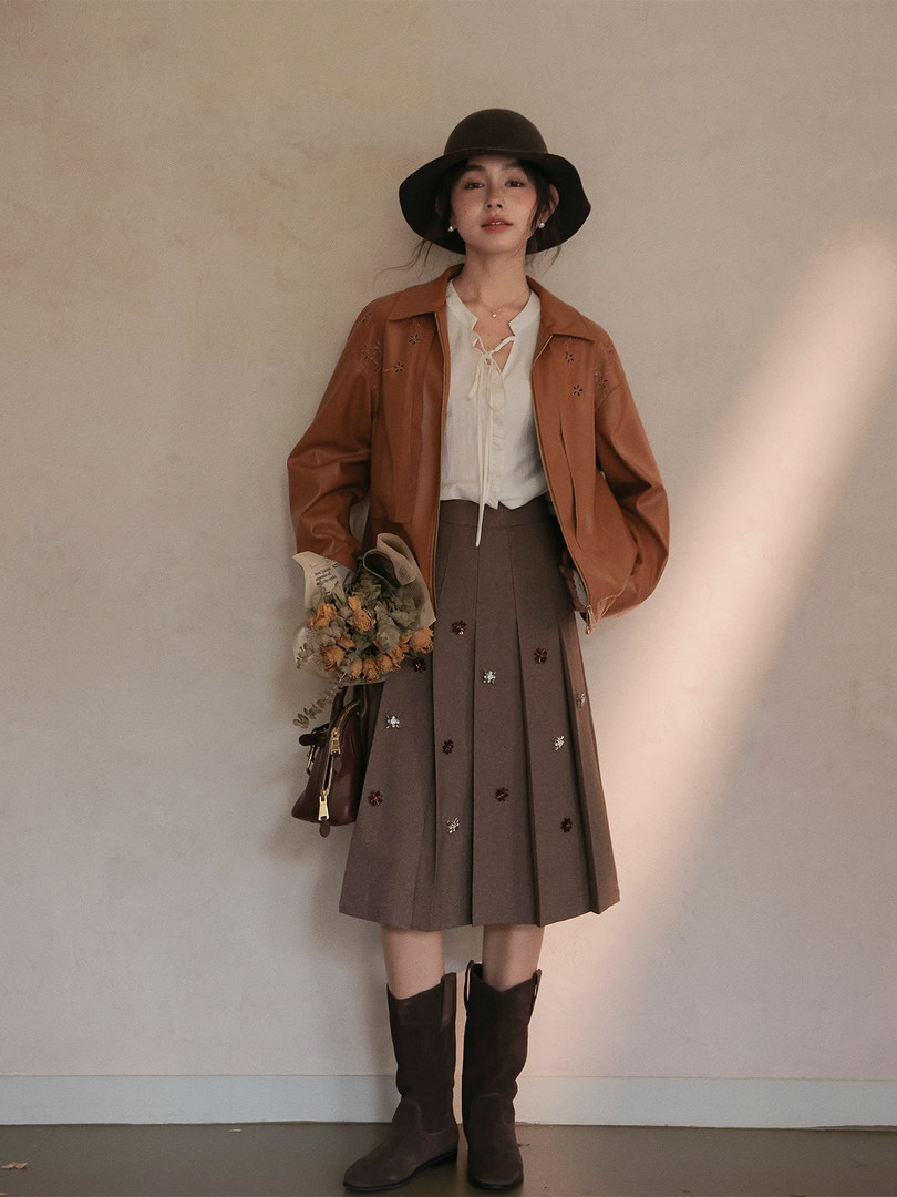 Woman wearing a brown jacket, pleated skirt, hat, and boots