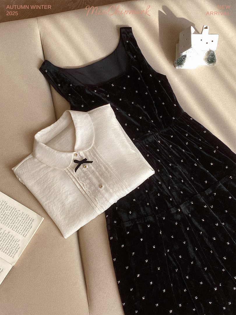Black sleeveless dress and white collared blouse laid flat on a beige background