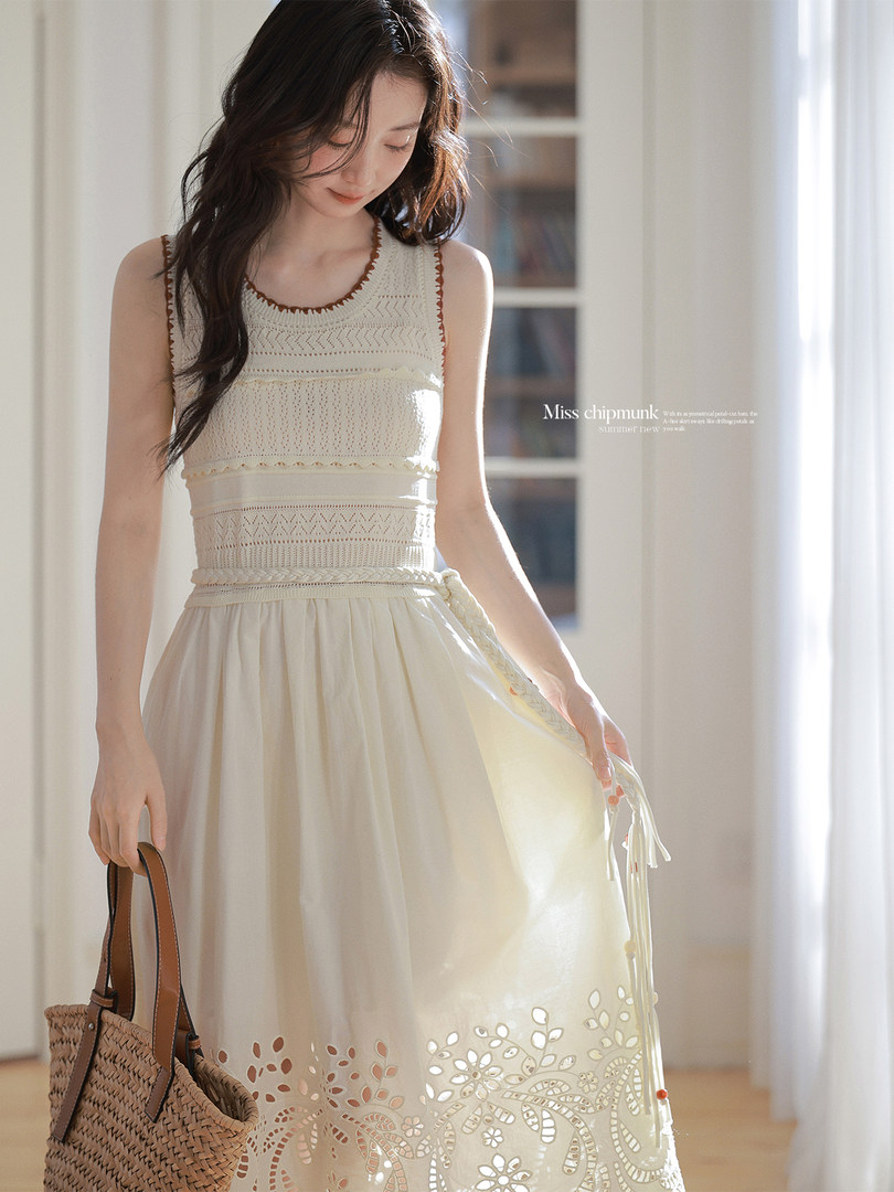 Model wearing a cream sleeveless dress with cutout floral hem and woven handbag