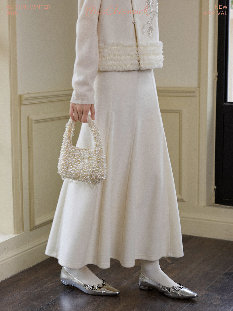 Model wearing a cream winter outfit with a pearl handbag and silver flats
