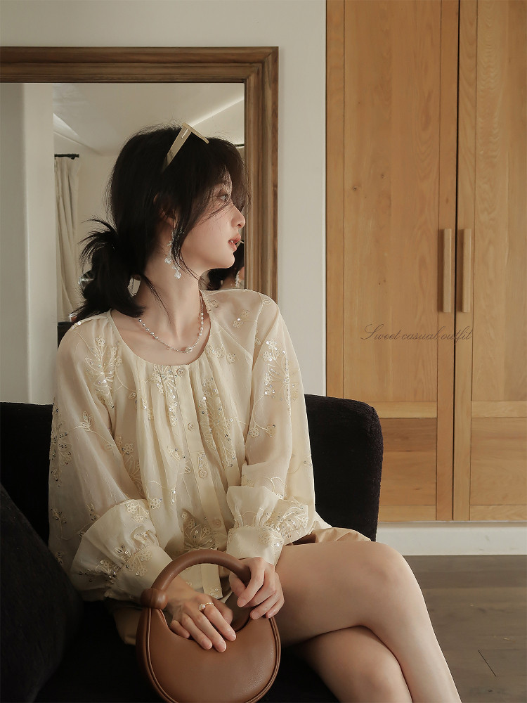 Cream embroidered sheer blouse worn by a model seated indoors