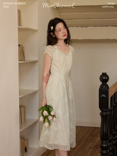 Model wearing a light cream floral dress indoors with flowers in hand
