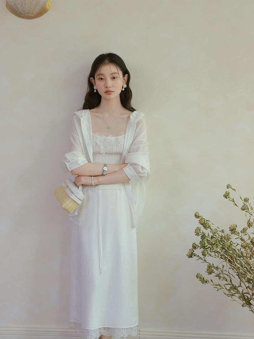 Woman wearing a white lace-trim dress with a sheer cardigan and small woven bag