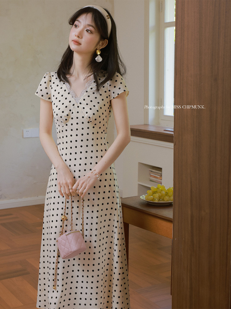 Woman wearing a cream polka dot midi dress with a small pink handbag indoors