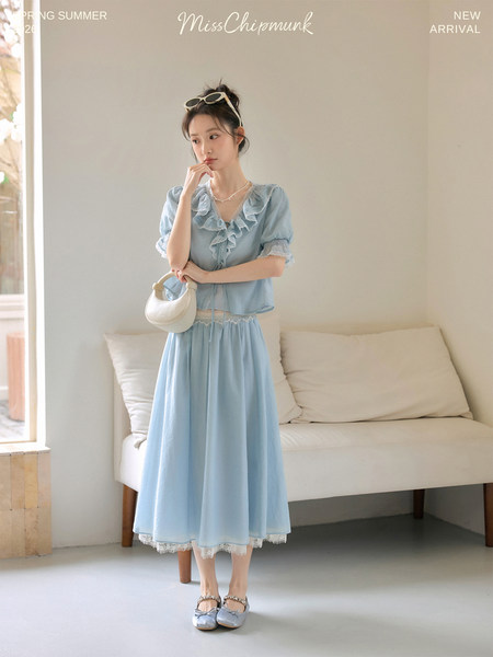 Model wearing a light blue ruffled two-piece outfit with a small white handbag