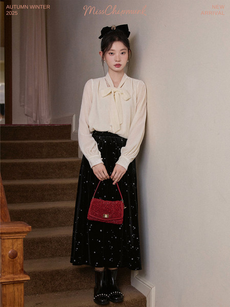 Model wearing a cream bow blouse with a black star-pattern skirt and red handbag