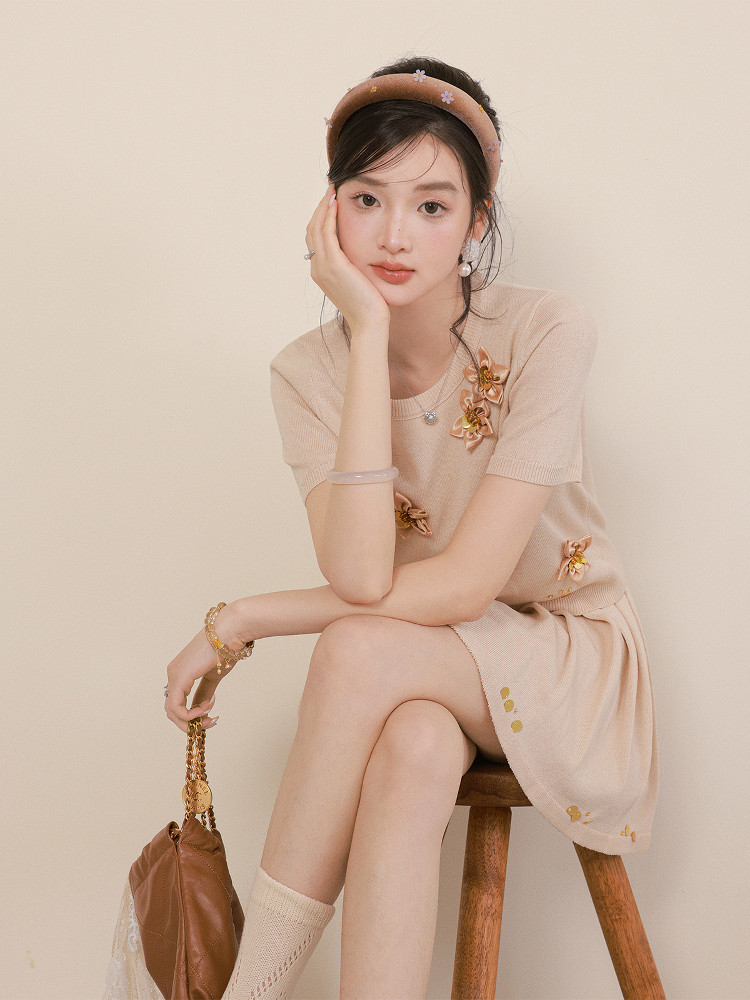 Model wearing a beige short-sleeve knit dress with floral appliqué and matching headband
