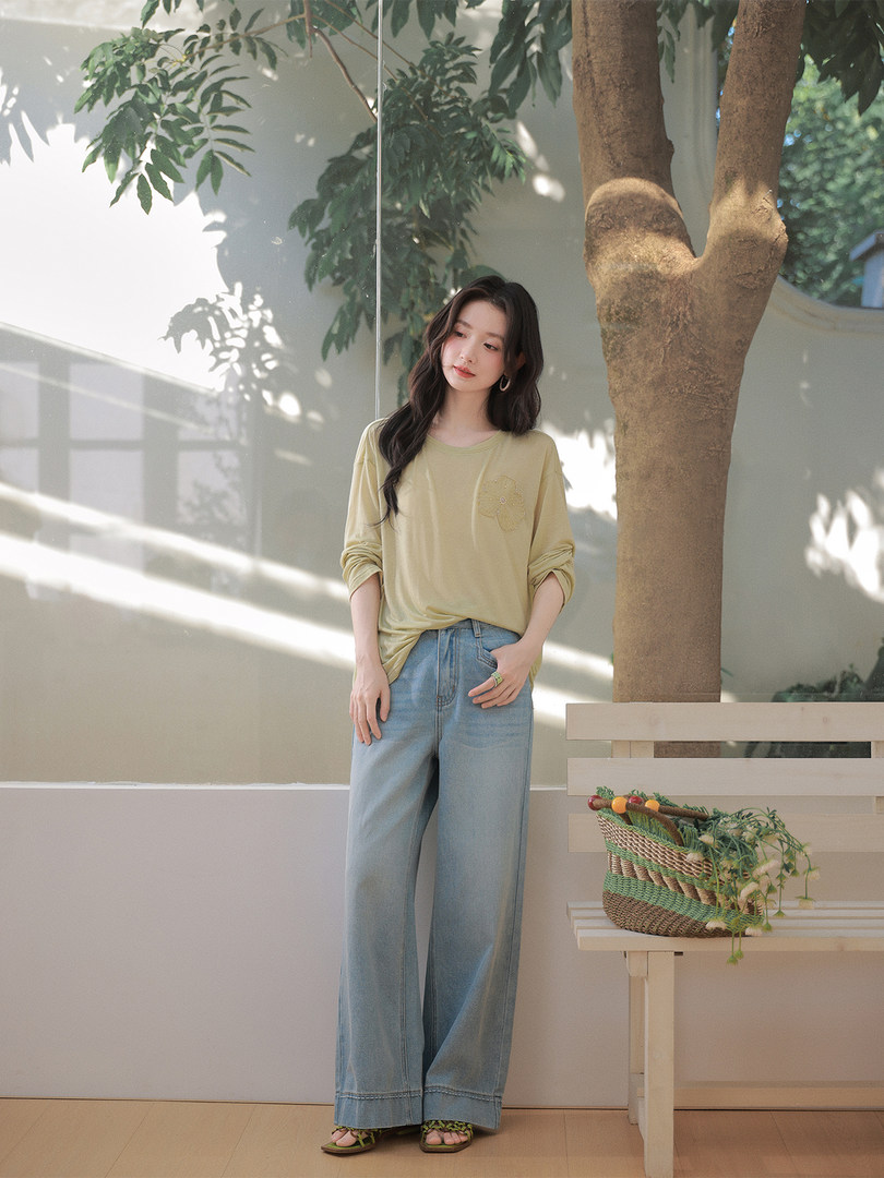 Woman wearing a light yellow long-sleeve top with wide-leg blue jeans