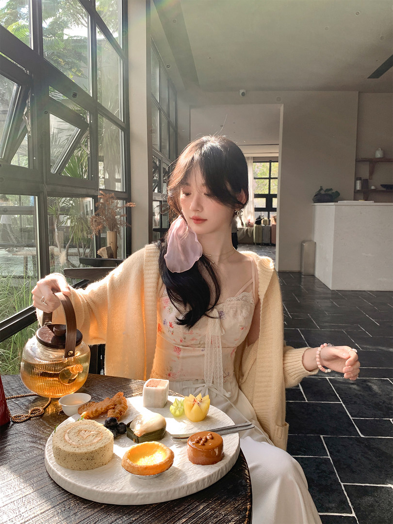 Woman wearing a cream cardigan over a floral dress while seated at a table with desserts