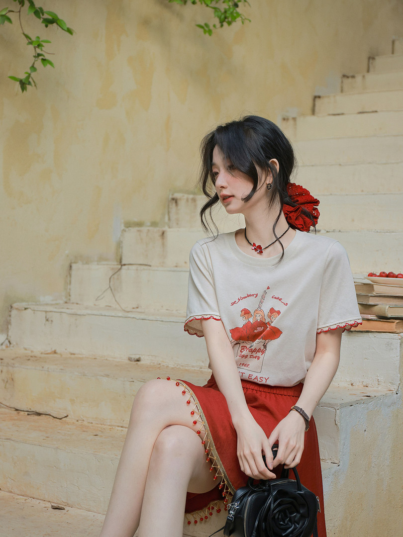 Model wearing a white graphic T-shirt and red skirt outfit