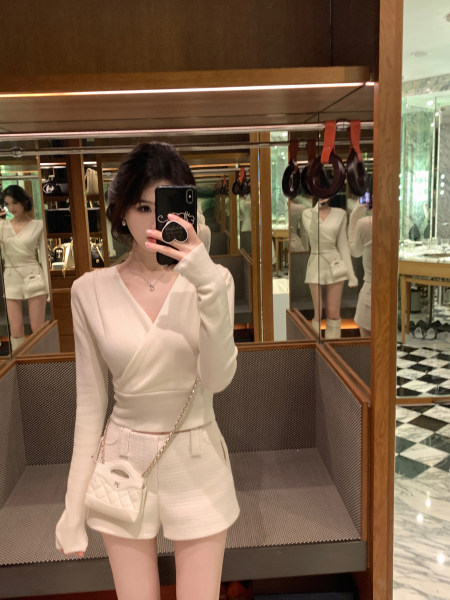 Woman taking mirror selfie wearing white wrap top and matching shorts with small handbag