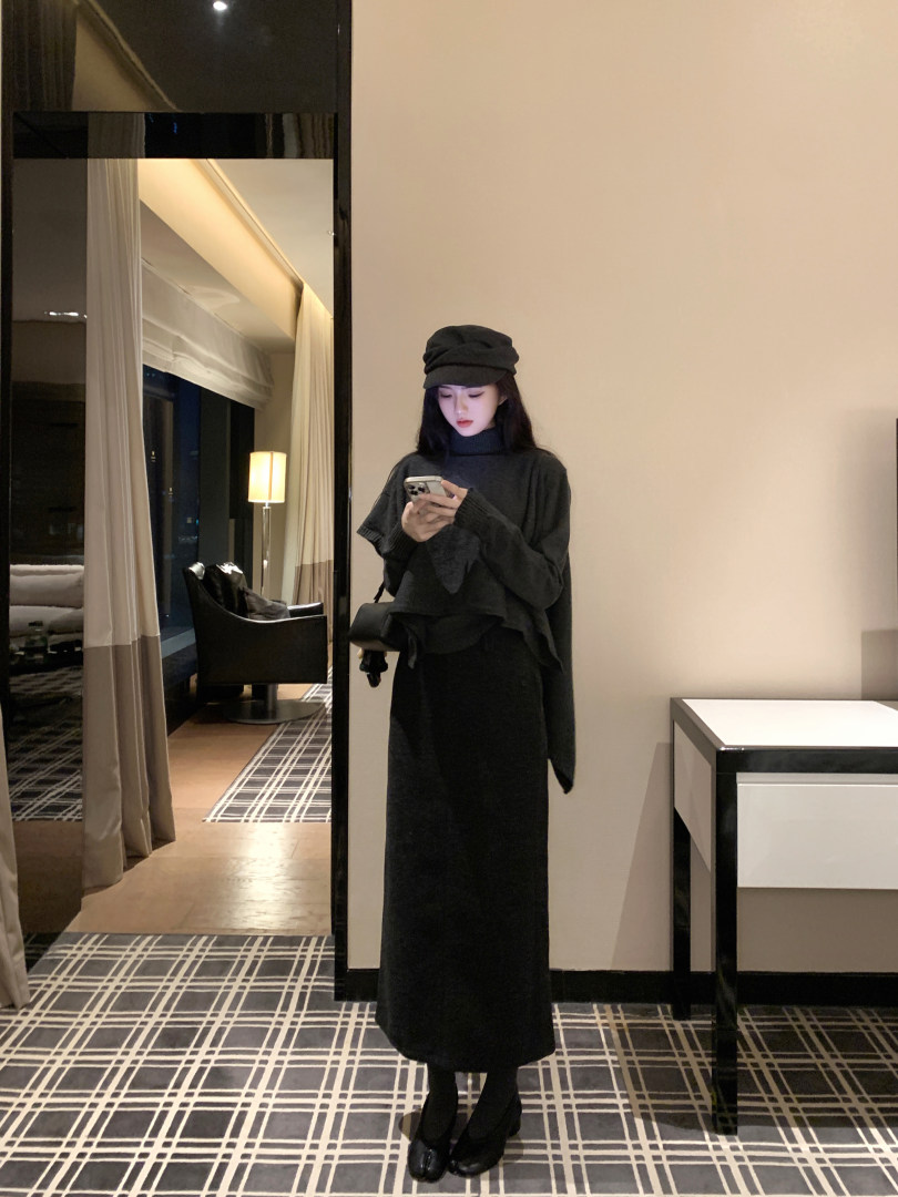 Woman wearing black turtleneck sweater, long black skirt, and black beret, taking mirror selfie in hotel room