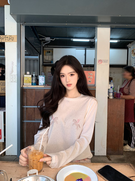 Woman wearing a light-colored long-sleeve shirt with small printed designs, holding a drink at a café.