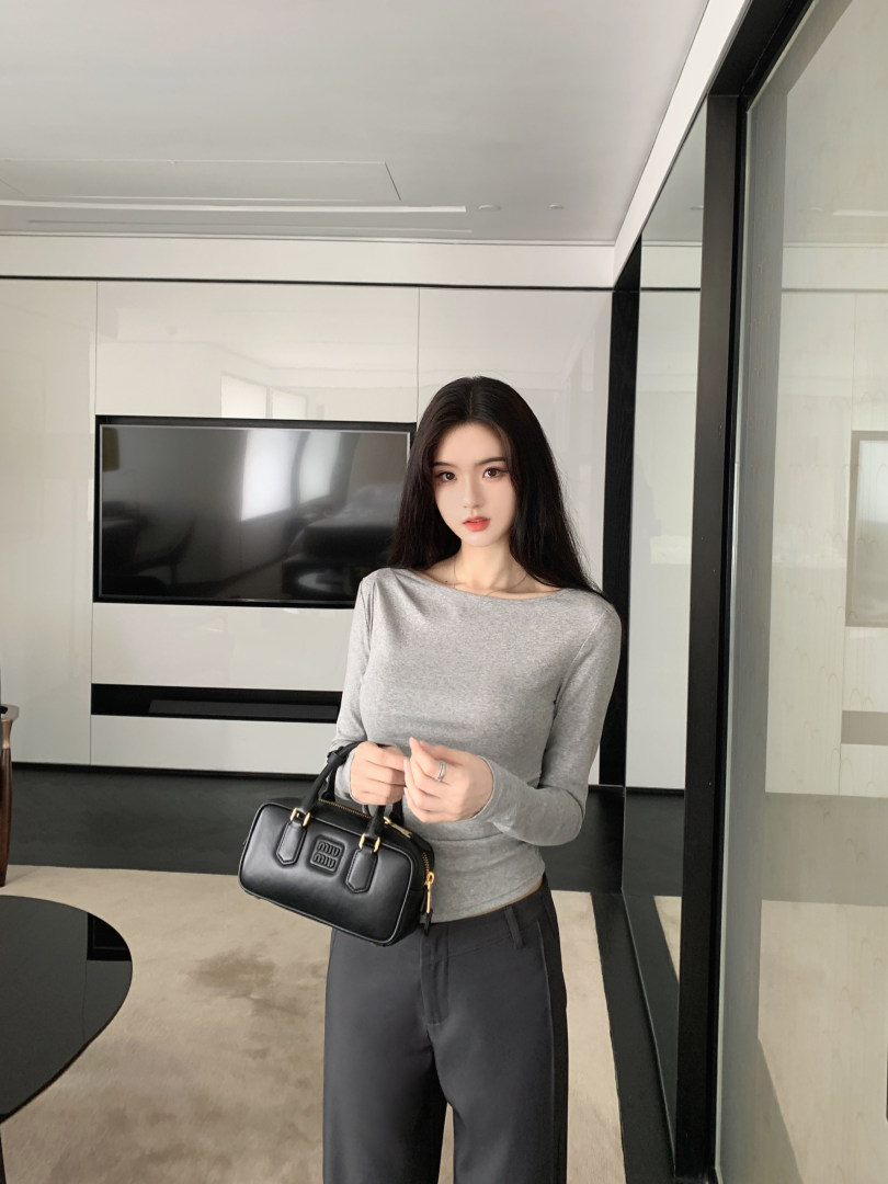 Woman wearing a gray long-sleeve top and black pants, holding a black handbag.