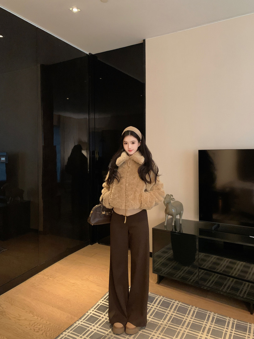 Woman wearing a beige fuzzy jacket, brown wide-leg pants, and a headband, holding a brown handbag.