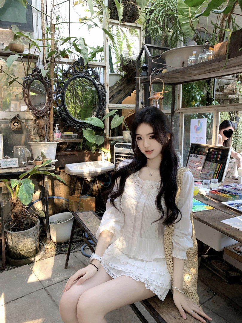 Woman wearing a white lace dress sitting in a plant-filled room