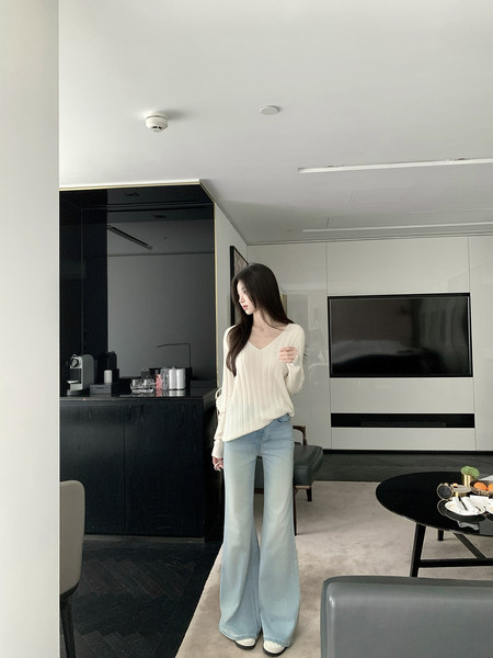 Woman wearing a white ribbed sweater and light blue wide-leg jeans in a modern living room.