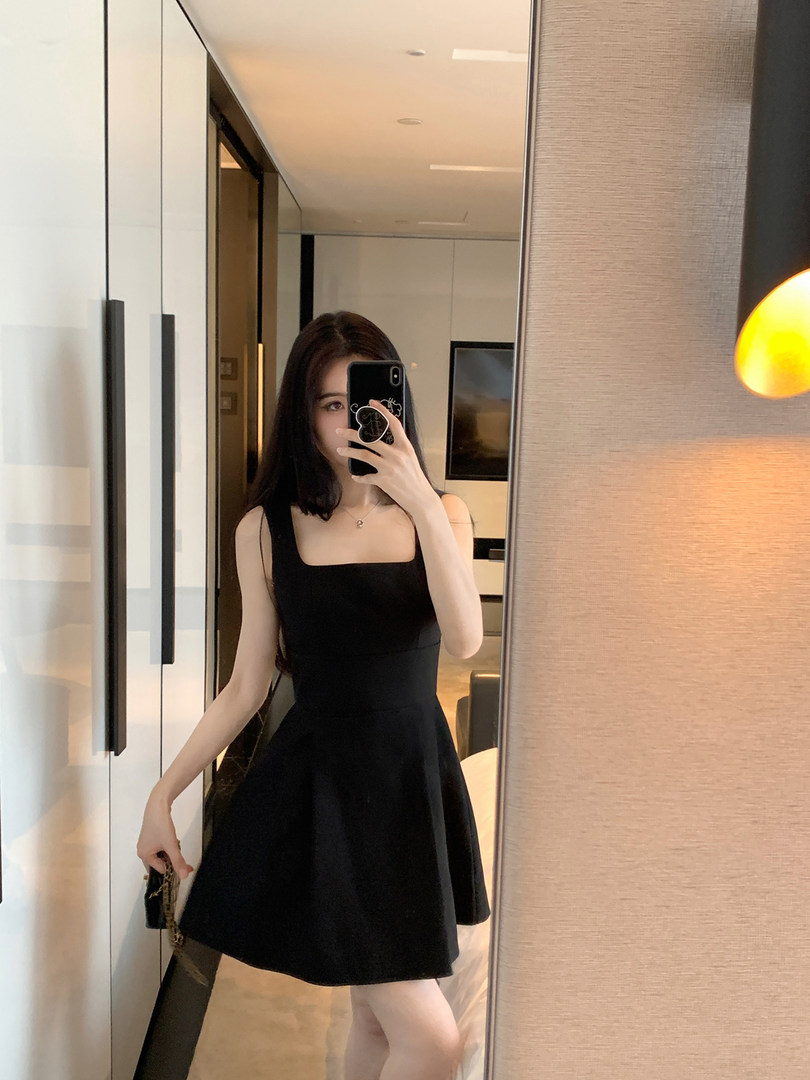 Woman taking mirror selfie wearing black sleeveless dress with square neckline and flared skirt