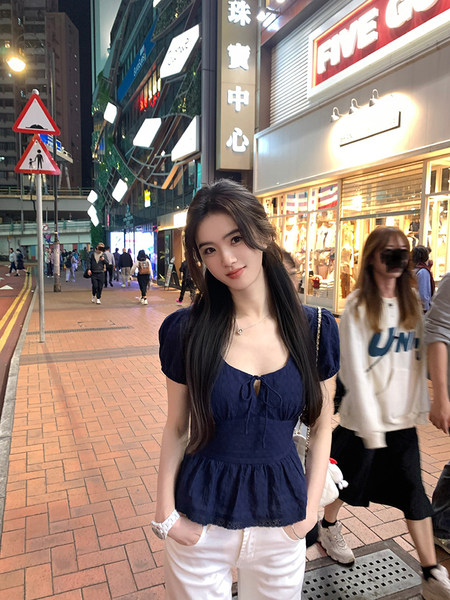 Woman wearing a navy blue peplum top and white pants on a city street at night.