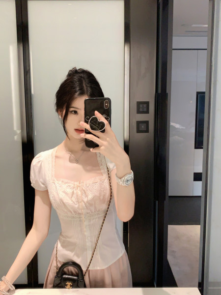 Woman taking mirror selfie wearing a light pink lace top with puff sleeves and a black handbag.