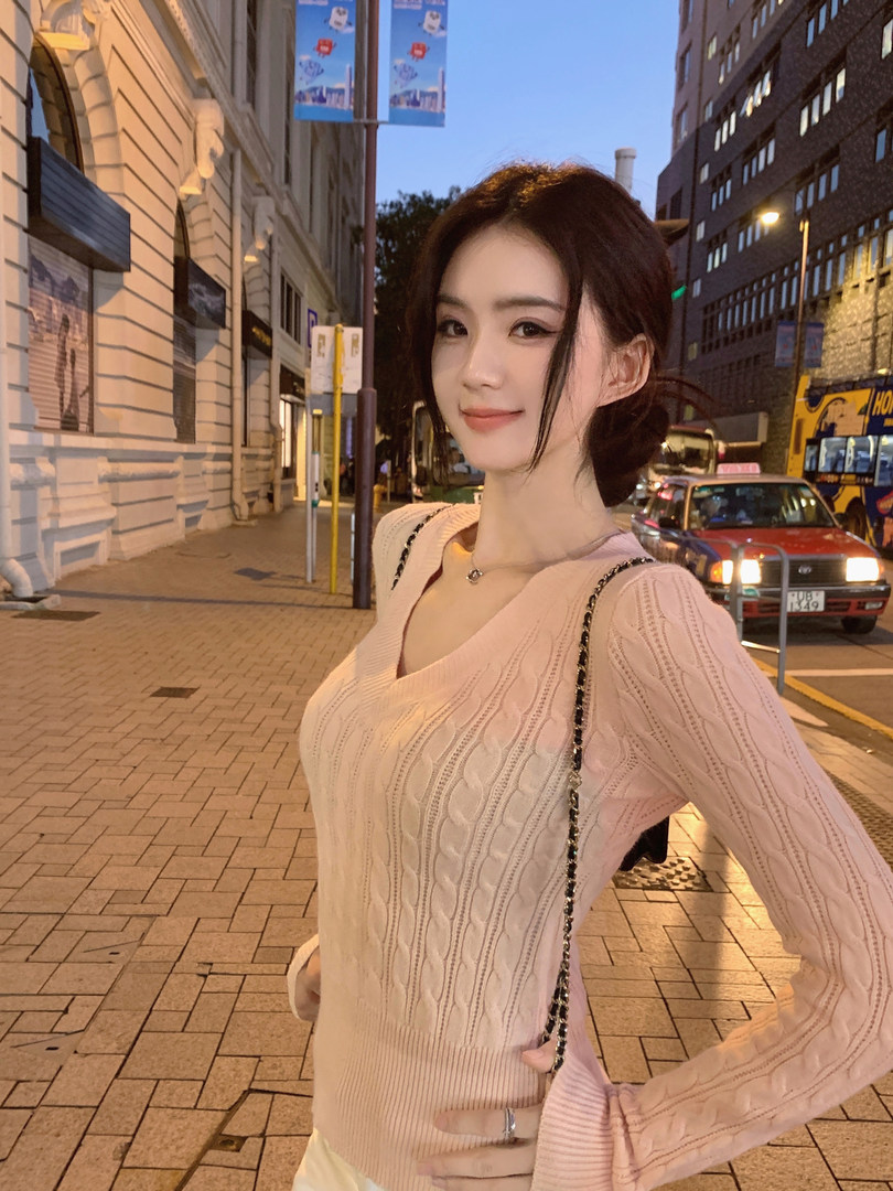 Woman wearing a pink knitted sweater on a city street at dusk