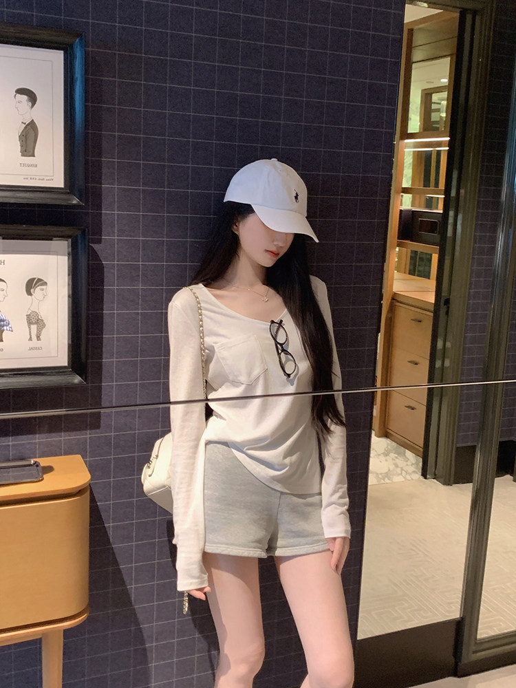 Woman wearing white long-sleeve top, gray shorts, and white cap with sunglasses hanging on her shirt.