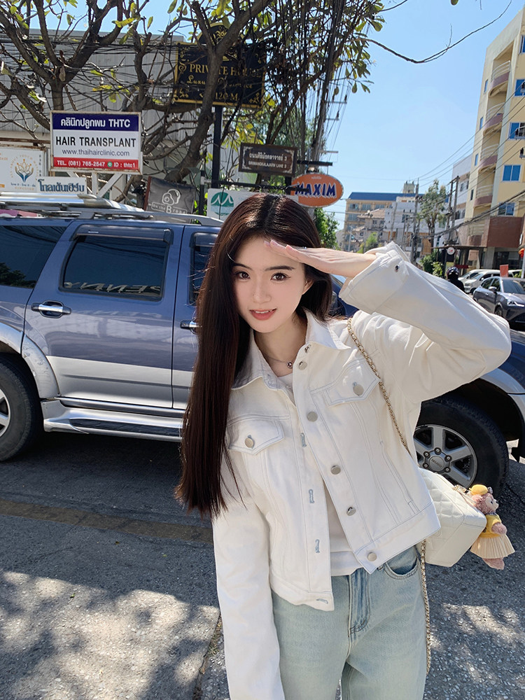 Woman wearing white denim jacket outdoors on a sunny street
