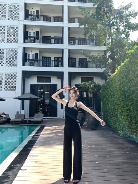 Woman wearing black sleeveless top and wide-leg pants by a poolside
