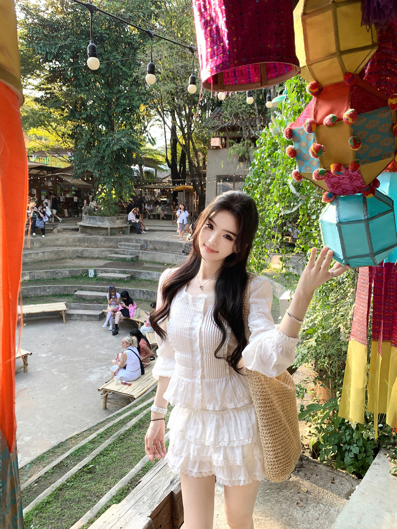 Woman wearing a white ruffled dress with lace details, standing outdoors near colorful lanterns.